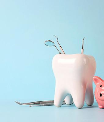 Piggy bank next to model of tooth holding dental tools