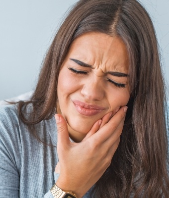 Woman who needs emergency dentist in Claremore holding her cheeks in pain