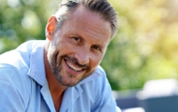 Older man in light blue shirt smiling outdoors