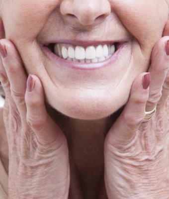 Smiling senior woman holding her cheeks after replacing missing teeth in Claremore