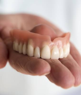 Hand holding a full upper denture