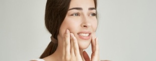 Woman with ponytail holding her cheeks in pain