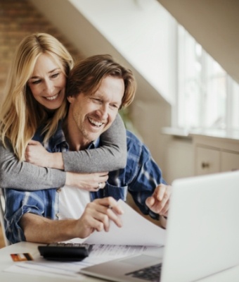 Woman hugging a man who is sitting at table with laptop