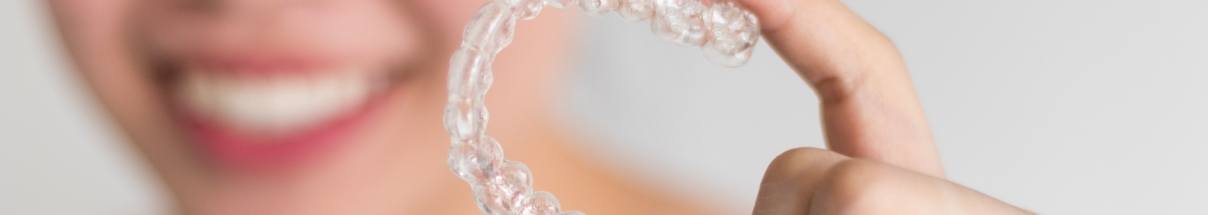 Close up of smiling person holding SureSmile clear aligner in Claremore